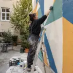 Osoba oslikava geometrijski motiv na zidu gradskog dvorišta